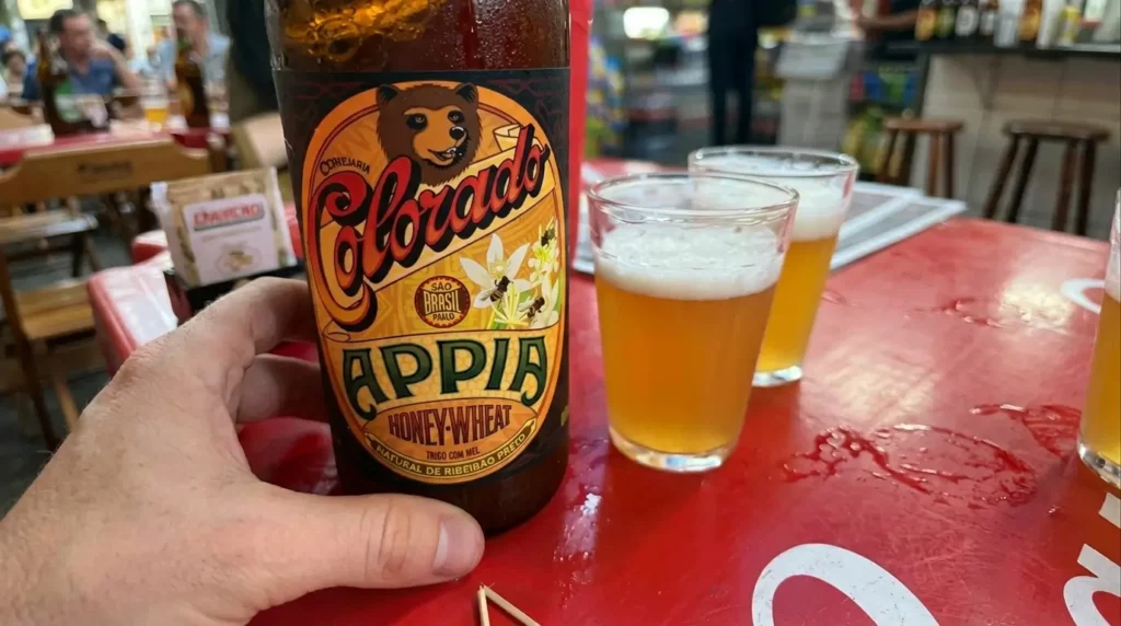 cerveja colorado appia é boa - Close-up macro no líquido dourado e levemente turvo da cerveja de trigo dentro da taça, mostrando as pequenas bolhas de carbonatação subindo até a camada grossa de espuma branca.